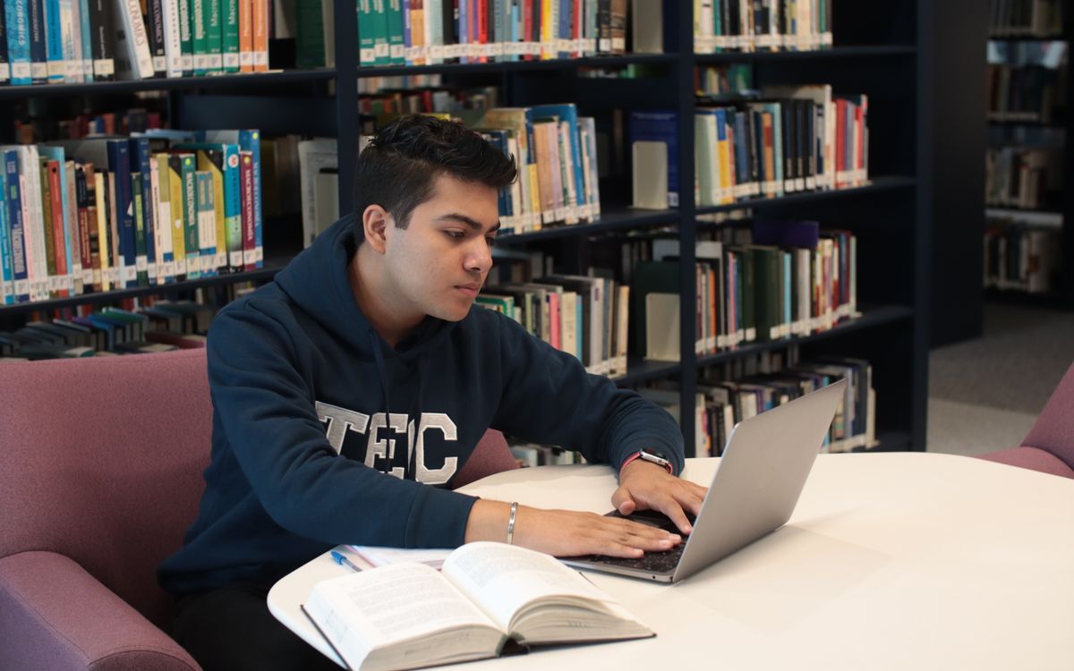 Doctoral candidate working on research with a laptop and books in a university library